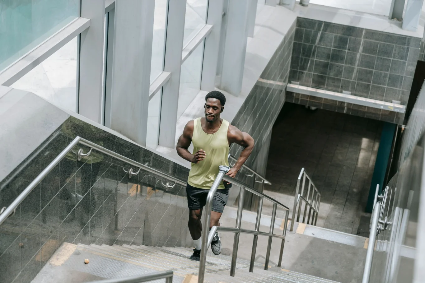 Athletic man in a yellow tank top running up indoor stairs during a cardio workout