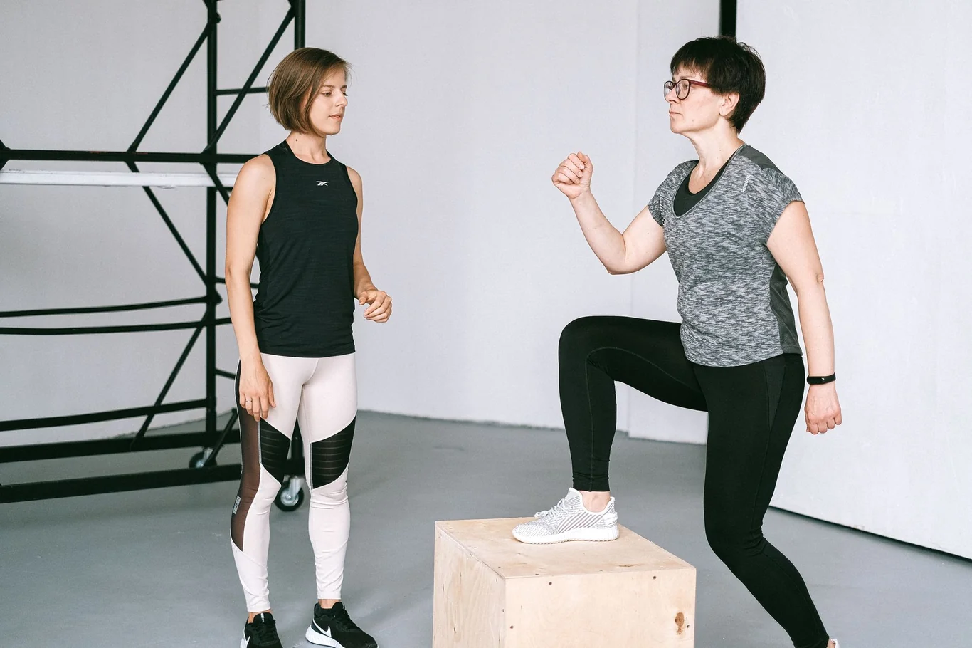 Woman stepping up on a plyo box during a glute-focused workout session with a trainer in a gym studio