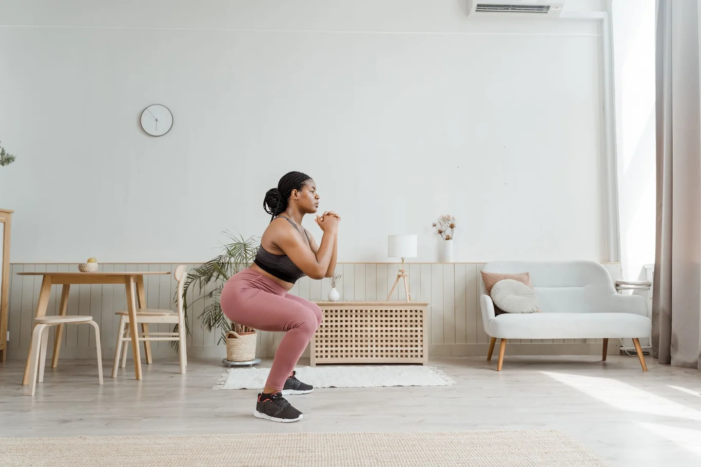 Woman performing a bodyweight squat in a bright, naturally lit home workout space