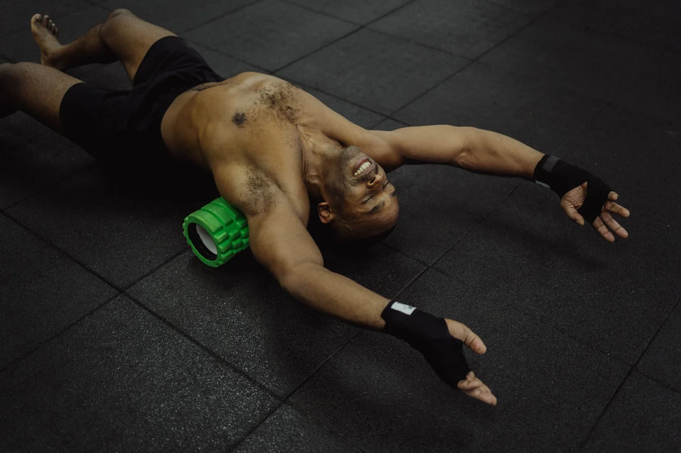 Man lying on gym floor using a green foam roller on his upper back for recovery