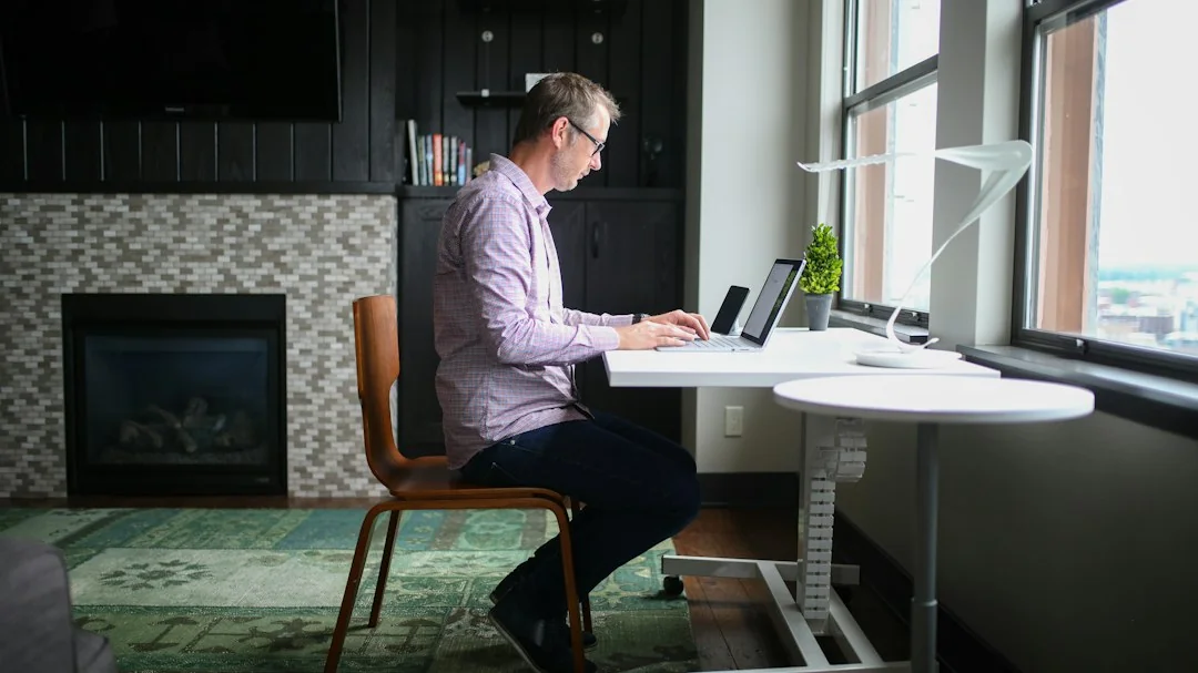 Man working at a white adjustable standing desk by a large window in a bright home office