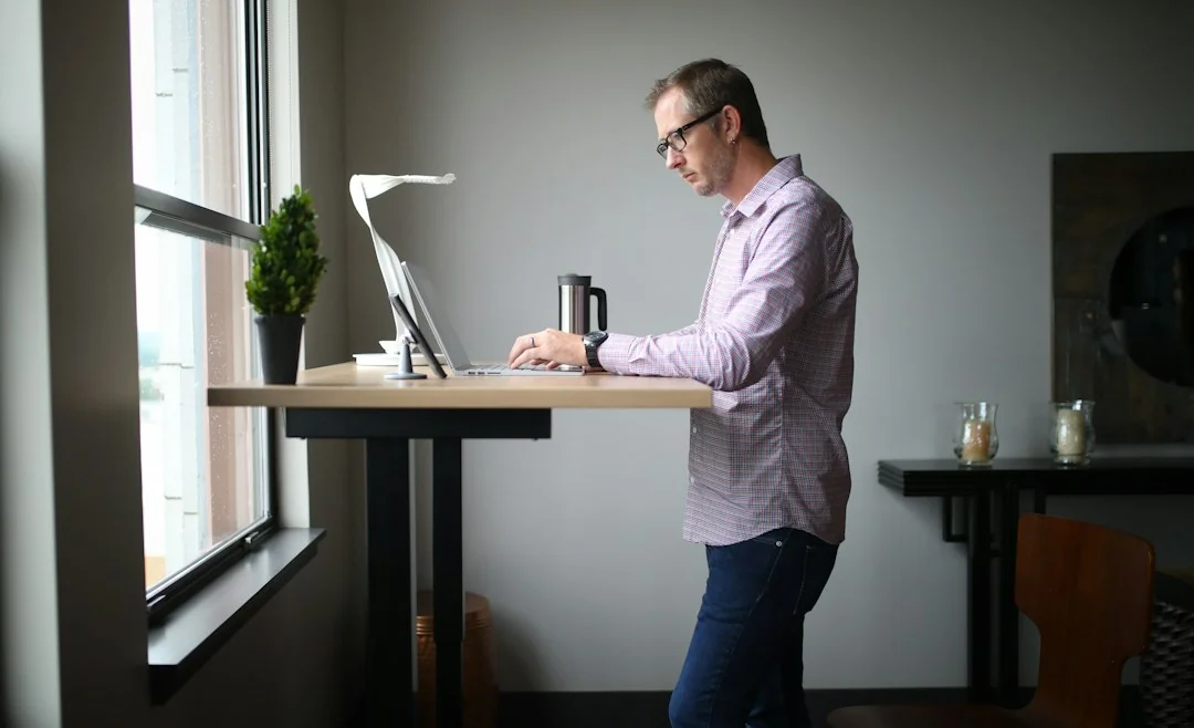 Man working at a standing desk with a laptop in a bright home office