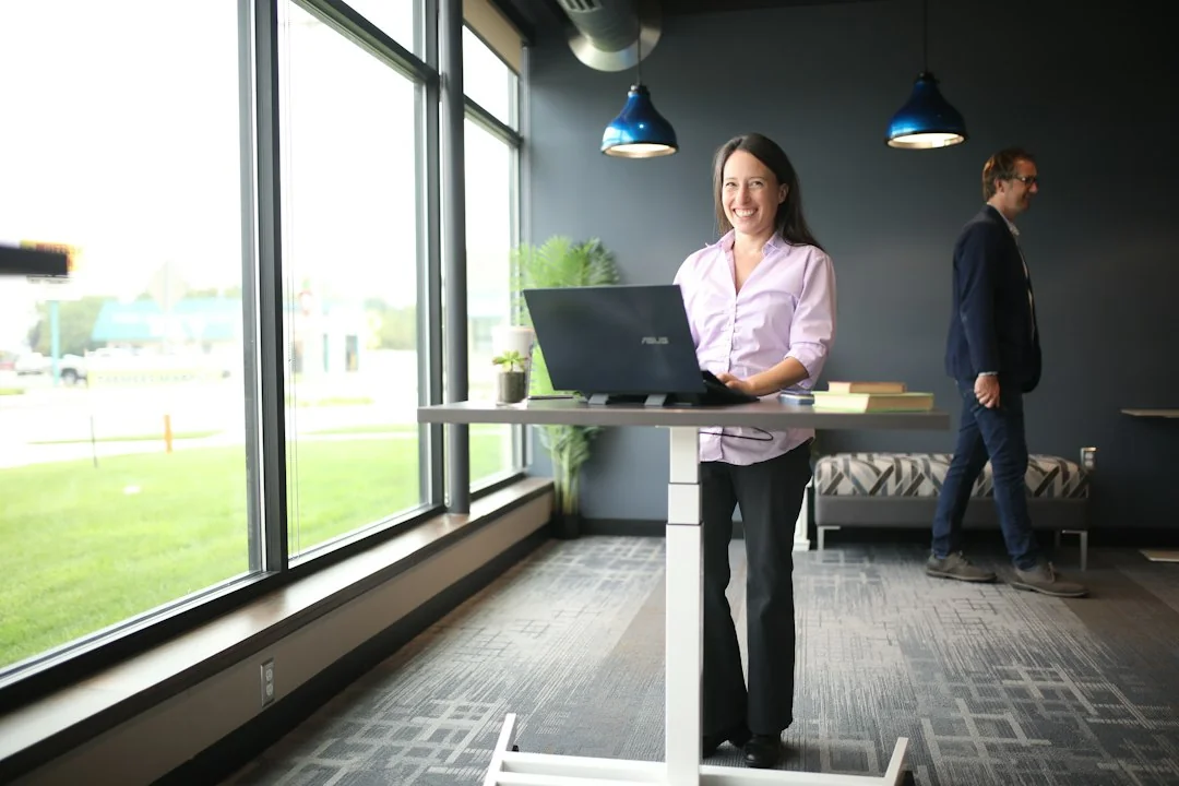 Woman working on a laptop at a standing desk in a bright office