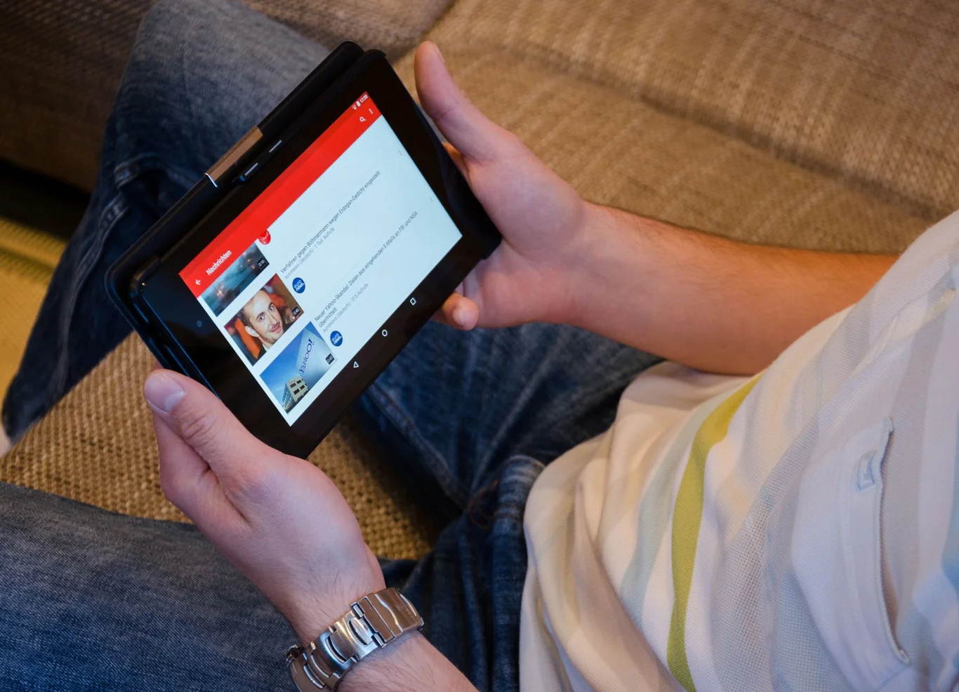 Person sitting on a couch holding a tablet with a video streaming interface on the screen