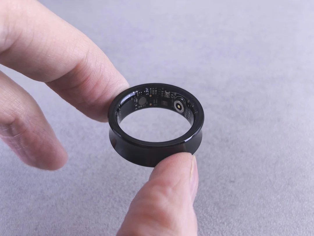 Black smart ring held between two fingers showing inner health sensors