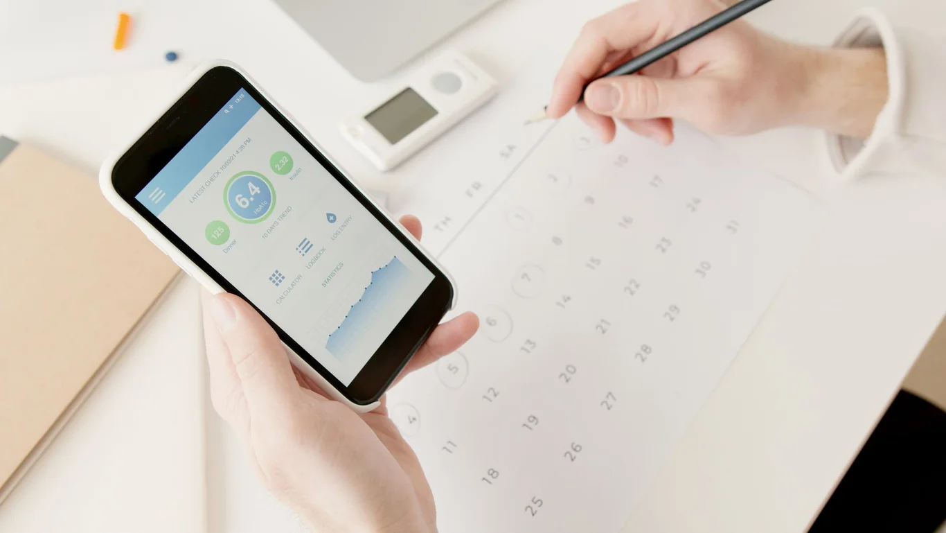 Hands holding a smartphone showing a health tracking app with a metric score and activity graph, calendar visible in