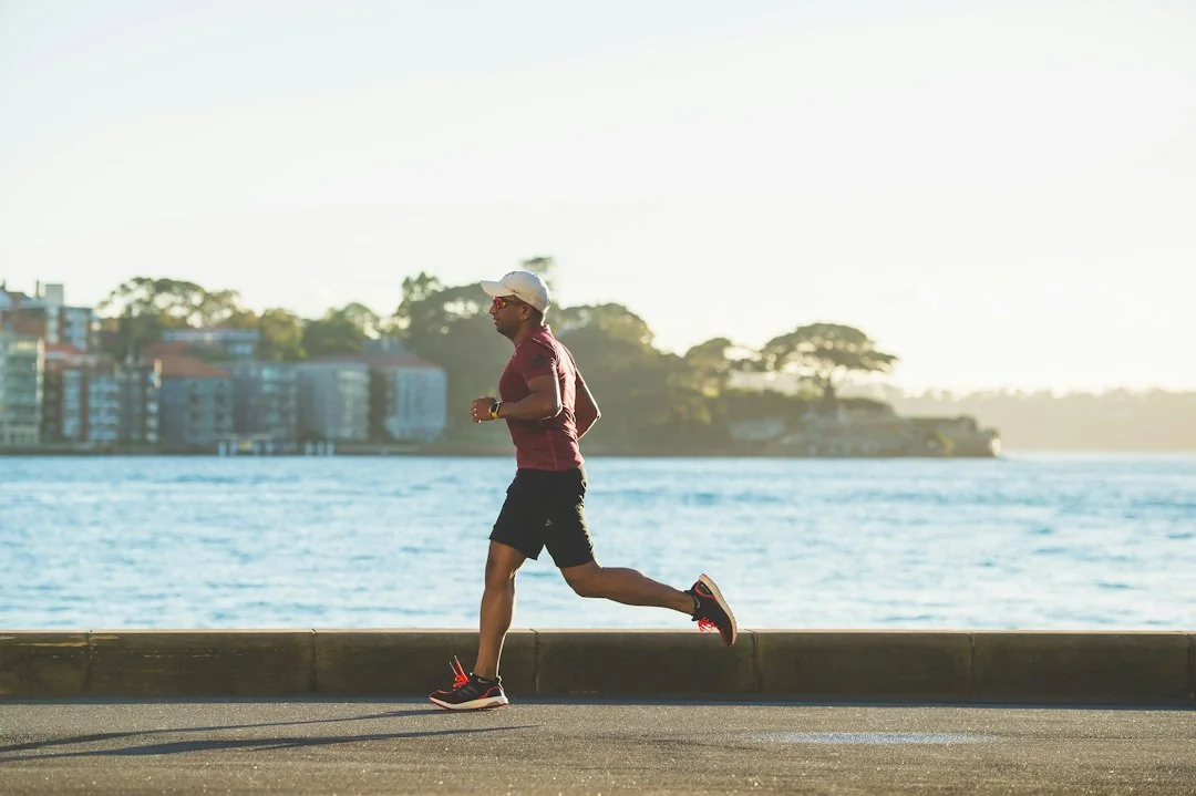 Man jogging along a waterfront path in warm morning sunlight