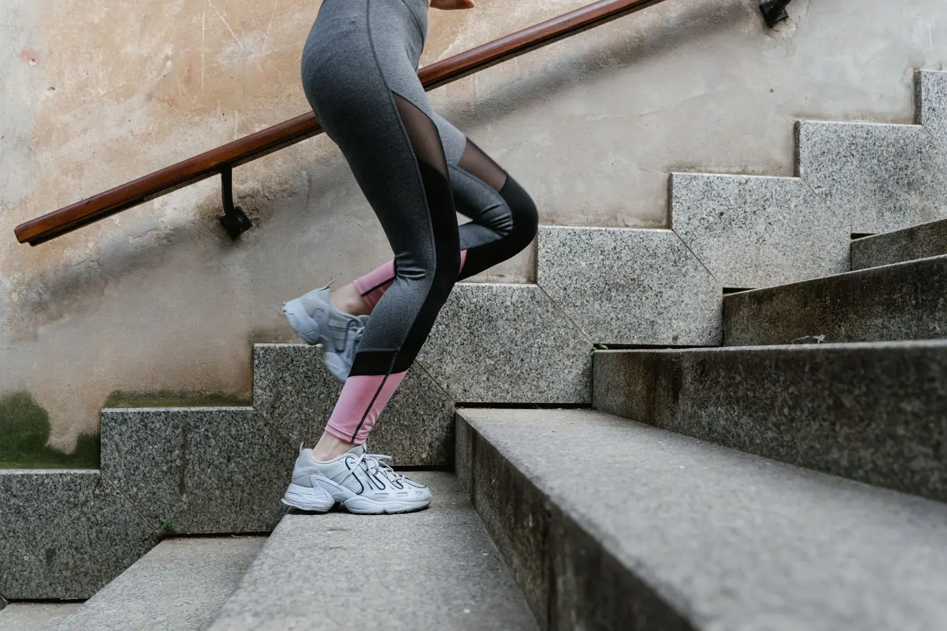 Woman in athletic leggings stepping up outdoor stone stairs during a workout
