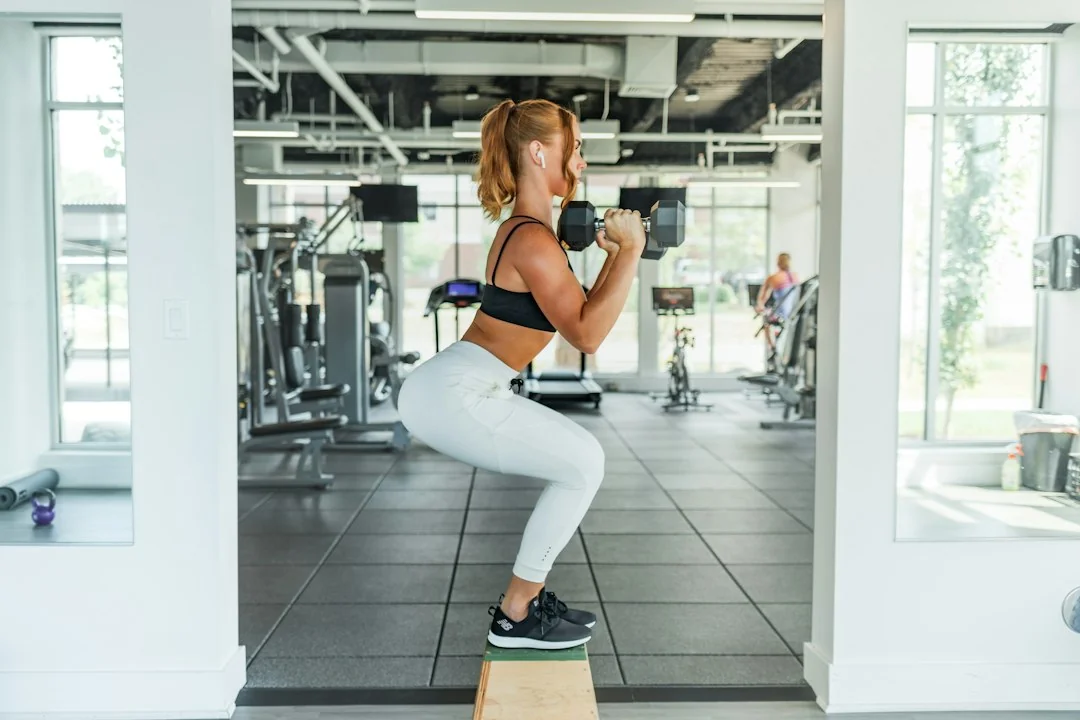 Woman holding dumbbells while squatting on a step box in a bright gym